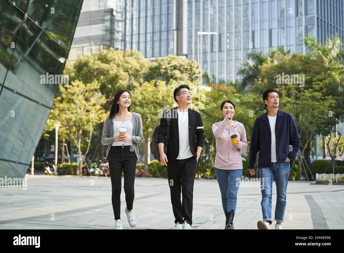 gruppo di quattro giovani asiatici che parlano chiacchierando mentre camminano per strada nella città moderna felice e sorridente Foto Stock