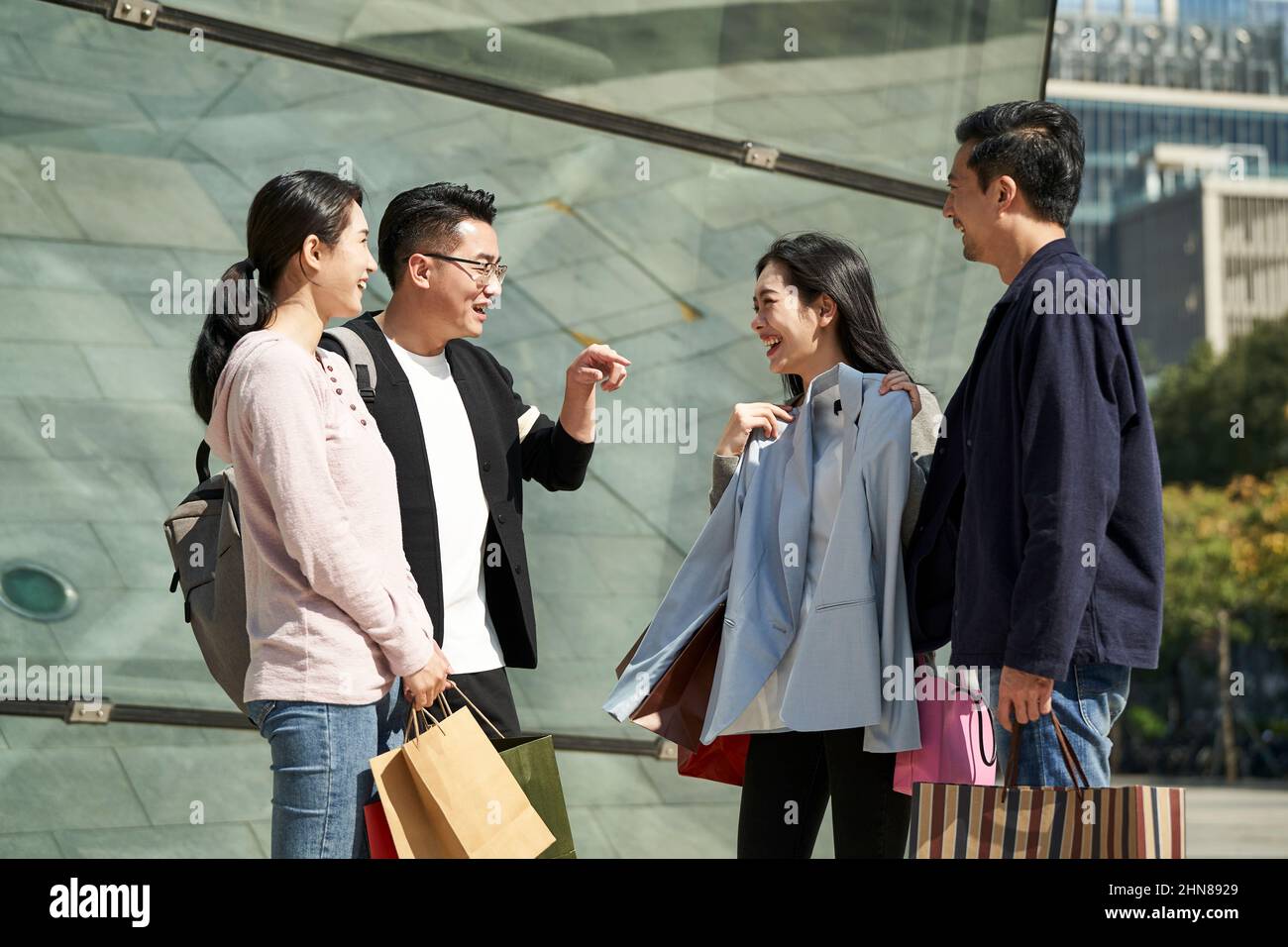gruppo di quattro giovani asiatici in piedi per strada parlando chiacchierando conversando durante il viaggio di shopping felice e sorridente Foto Stock