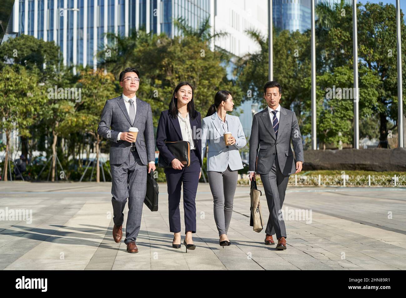 gruppo di quattro giovani uomini d'affari asiatici che camminano all'aperto in strada nella città moderna Foto Stock