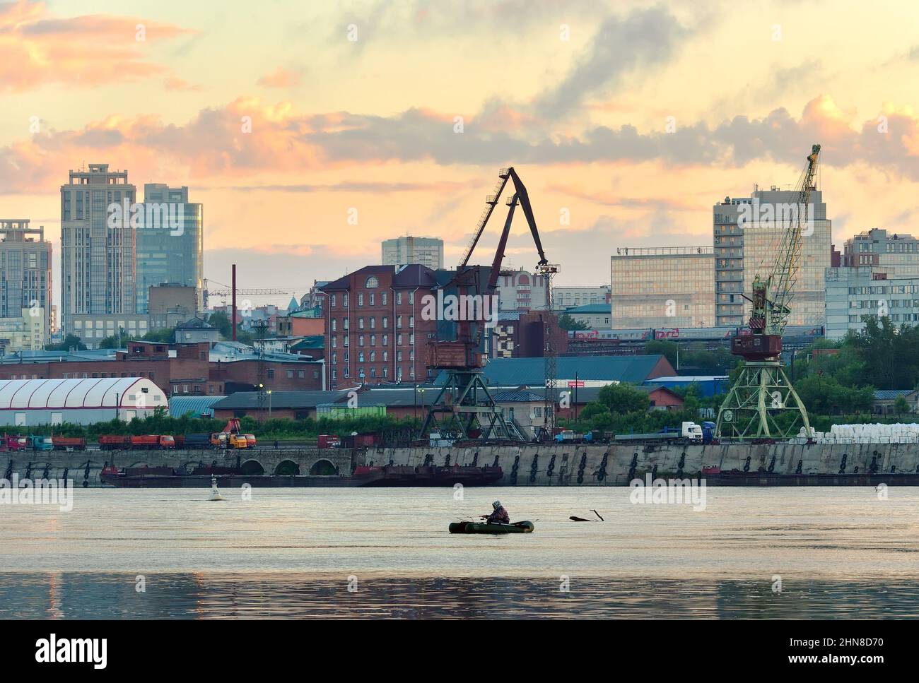 Novosibirsk, Siberia, Russia - 05.20.2020: Una barca gonfiabile nel mezzo del fiume OB, la riva di una grande città, gru portuali, case alte, Golden Foto Stock