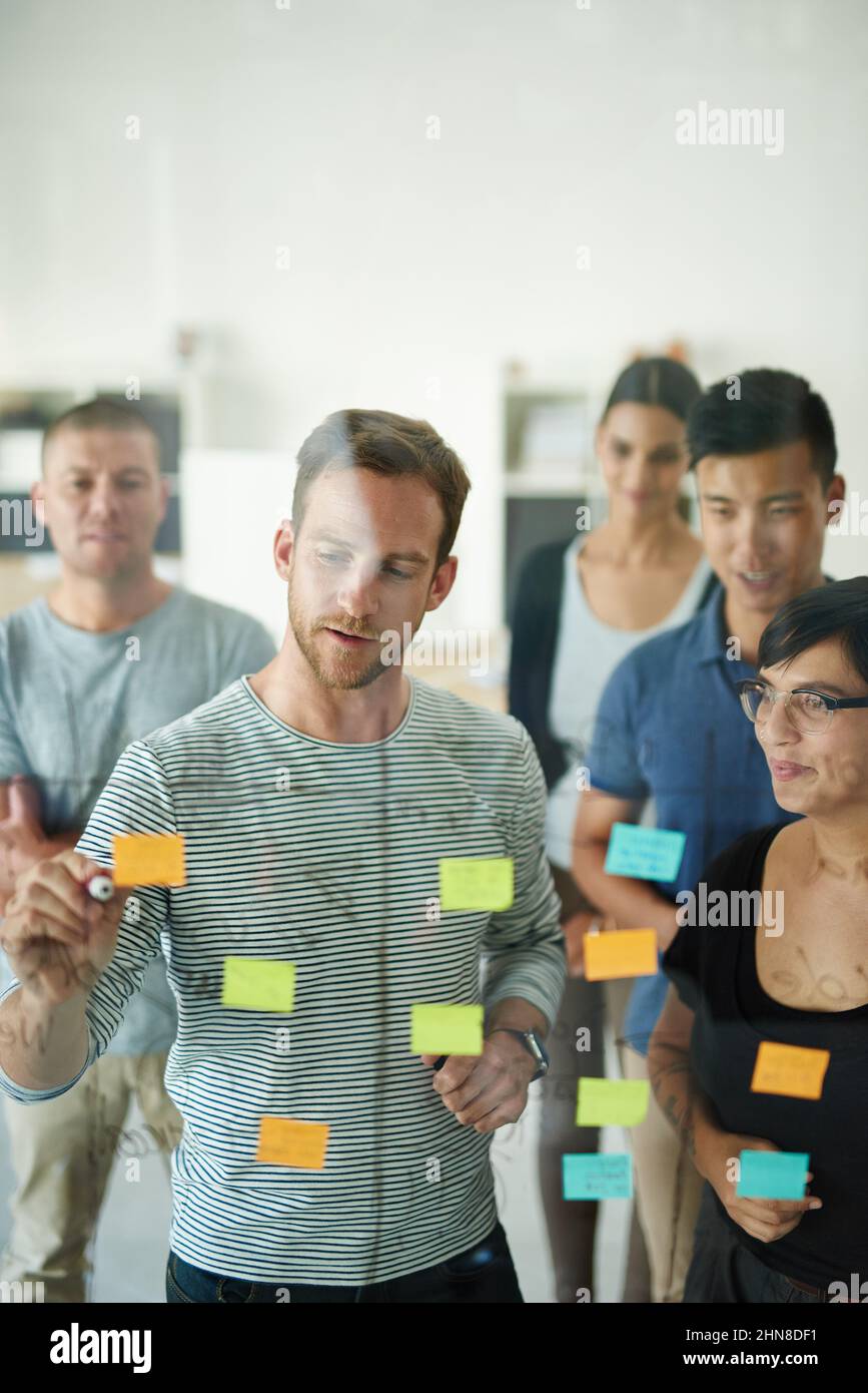 La pianificazione è il primo passo. Ripresa ritagliata di un gruppo di giovani designer che progettano su una tavola di vetro. Foto Stock