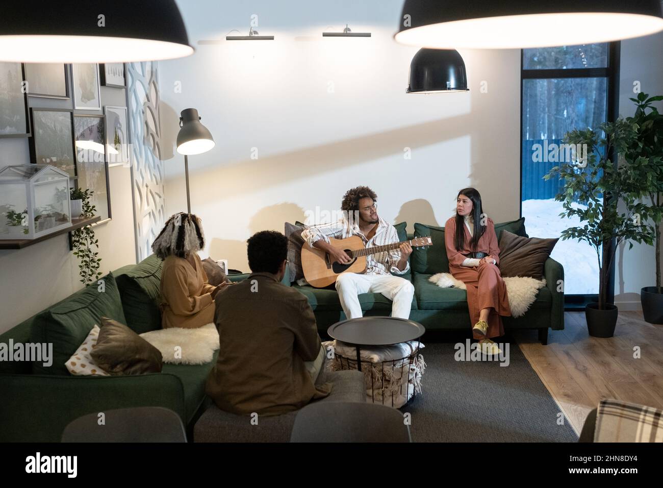 Gruppo di giovani seduti sul divano e cantando canzoni alla chitarra, trascorrono del tempo insieme a casa Foto Stock
