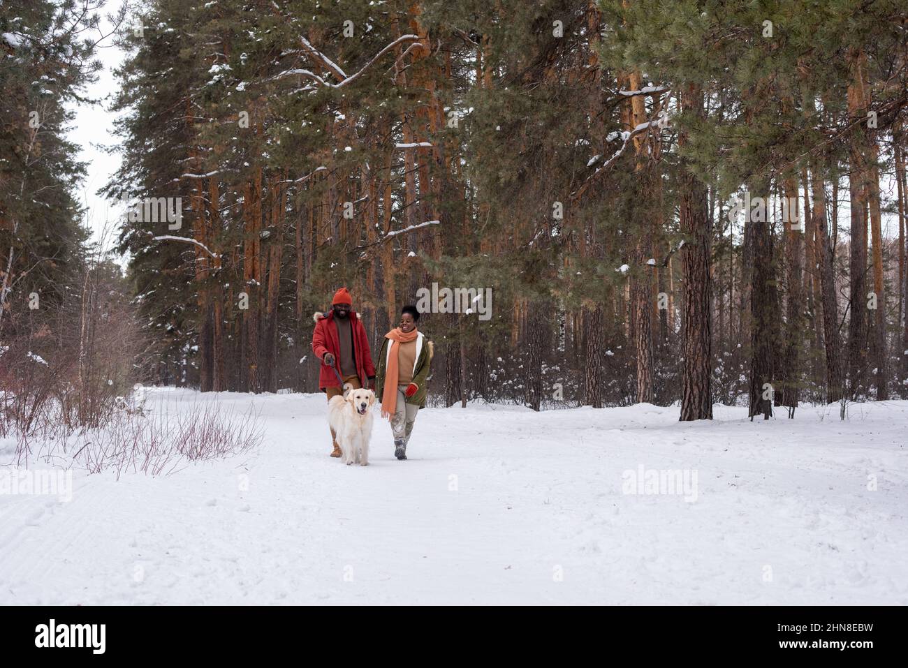 Coppia africana divertirsi con il loro cane durante la passeggiata nella foresta nel giorno d'inverno Foto Stock