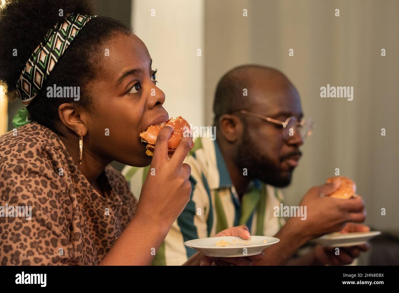 Giovane donna africana che mangia hamburger insieme al suo ragazzo per guardare il film a casa Foto Stock