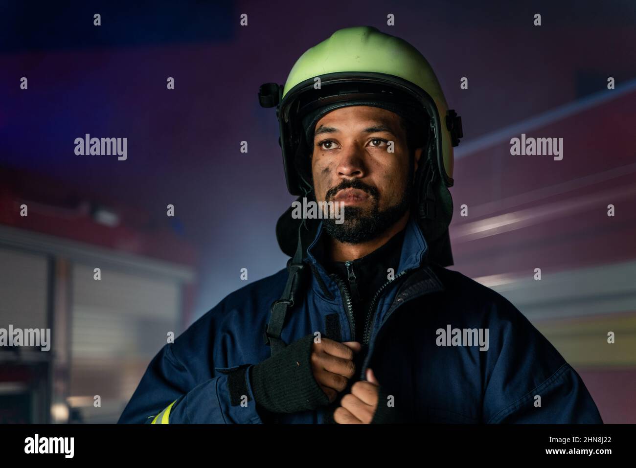 Ritratto di un uomo del pompiere sporco in servizio con camion del fuoco in background di notte. Foto Stock