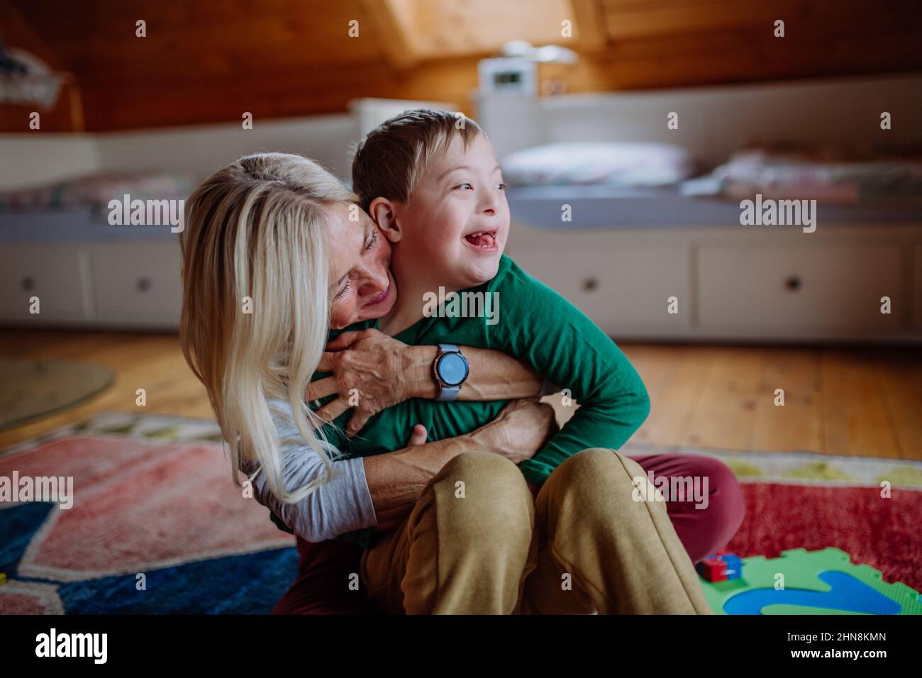 Ragazzo felice con sindrome di Down seduto a terra e abbracciato con la nonna a casa Foto Stock