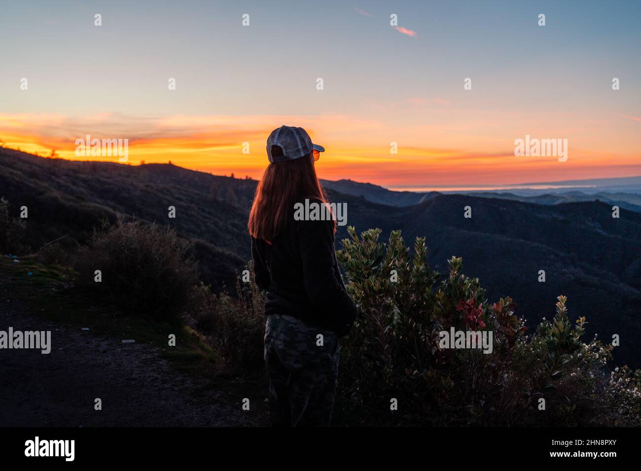 Donna si alza sul lato della montagna con vista del tramonto dietro di lei. Foto Stock