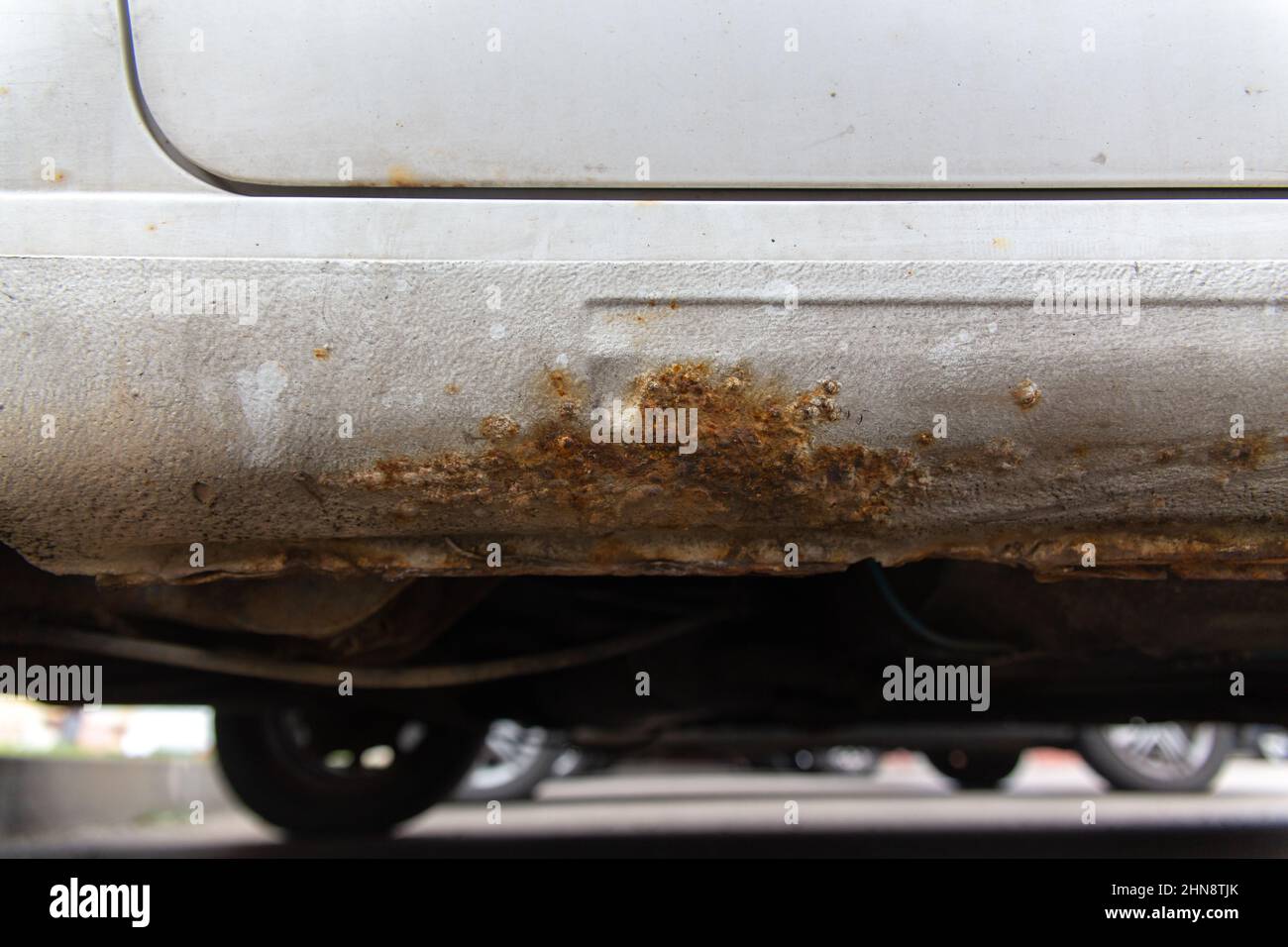 Ruggine sul lato della vecchia auto bianca. Foro di ruggine sulla vecchia superficie metallica verniciata usurata. Foto Stock