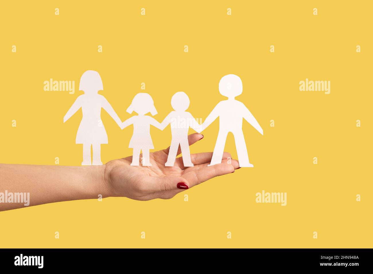 Profilo vista laterale primo piano della catena di famiglia della carta di tenuta della mano della donna, i rapporti fra i bambini ed i genitori. Studio interno girato isolato su sfondo giallo. Foto Stock