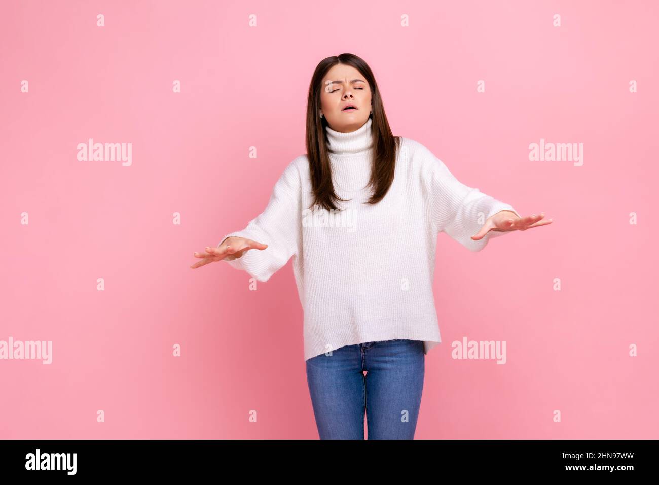 Ritratto di giovane donna disorientata che cammina con gli occhi chiusi e che tiene le mani per trovare la strada, indossando bianco stile casual maglione. Studio interno girato isolato su sfondo rosa. Foto Stock