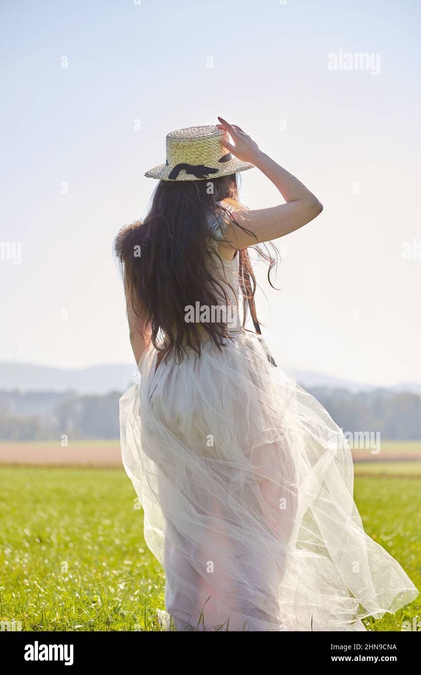 Giovane bella lunga capelli neri asiatica donna che indossa un abito romantico lilla in piedi in un campo d'erba retroilluminato Foto Stock