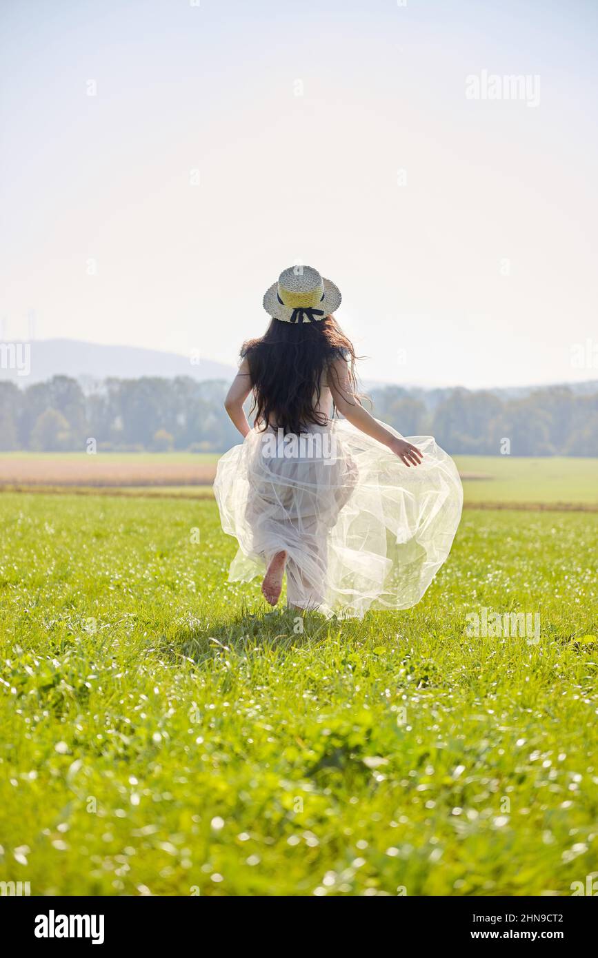 Giovane bella lunga capelli neri asiatica donna che indossa un abito romantico lilla in piedi in un campo d'erba retroilluminato Foto Stock