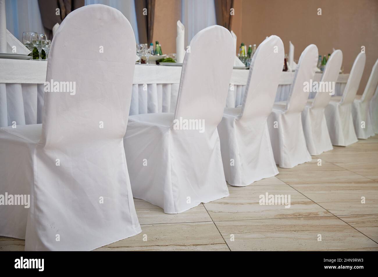 Sedie in coperte bianche in un ristorante vicino ad un tavolo set. Matrimonio Foto Stock