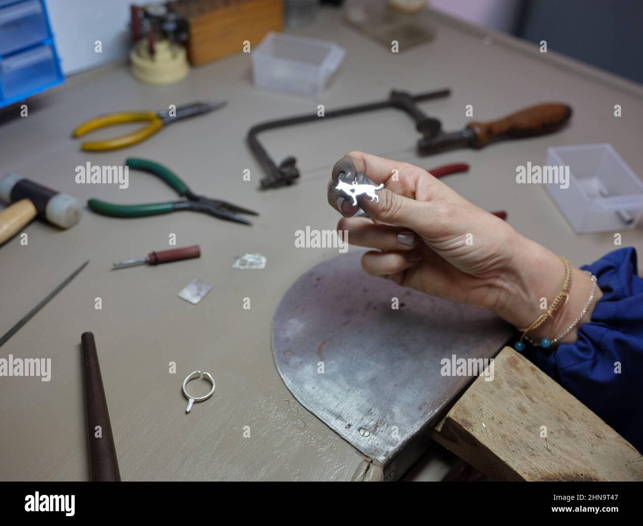 una donna adulta che tiene un fascino nella forma di un cane che ha appena fatto nel suo laboratorio di gioielli sul suo banco di lavoro Foto Stock