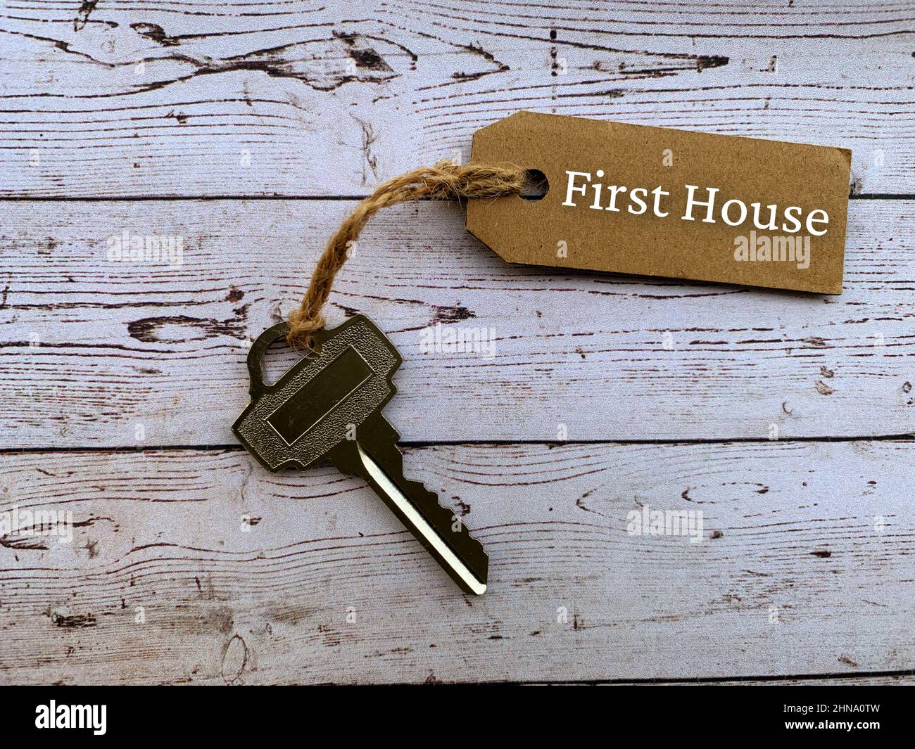 Testo su etichetta marrone con chiave casa e sfondo tavola in legno - prima casa. Concetto di proprietà. Foto Stock