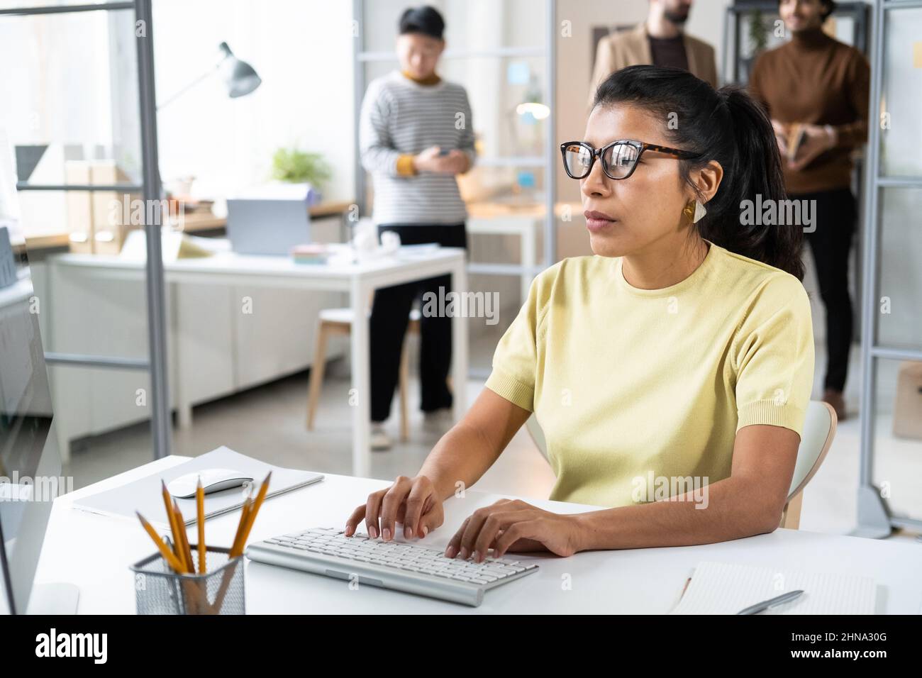 Donna d'affari seria in occhiali concentrandosi sul suo lavoro sul computer, si siede al tavolo e digitando sulla tastiera del computer Foto Stock
