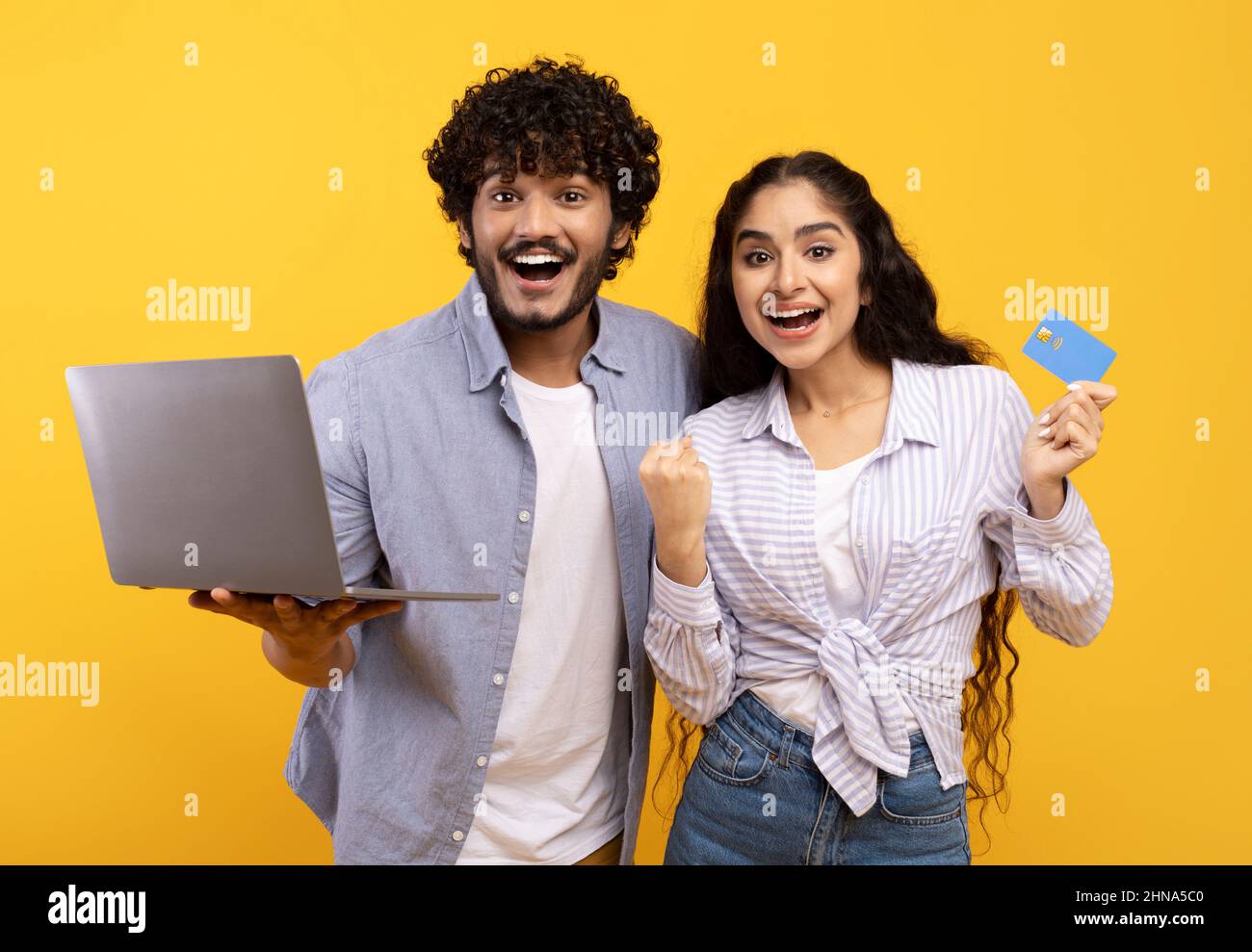 Sì, vendite enormi nel webstore. Una coppia indiana che tiene la carta di credito e utilizza il computer portatile, facendo il gesto del vincitore Foto Stock