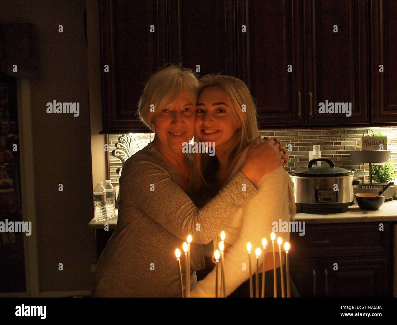 Nonna e nipote celebrano i compleanni reciproci in un ambiente soffocato di illuminazione e abbracciarsi l'un l'altro. Condividere un compleanno a 60 anni di distanza. Foto Stock