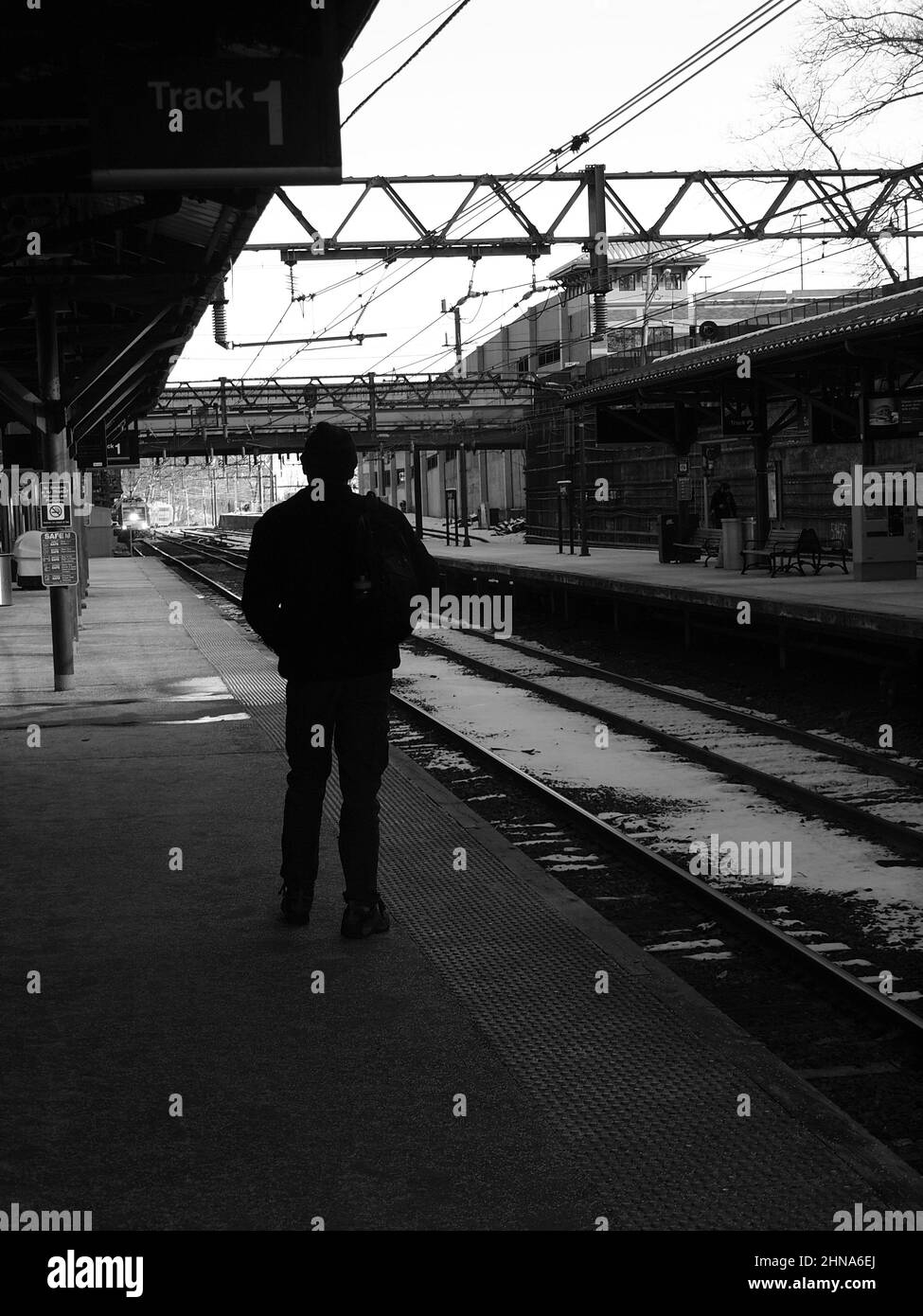 Figura oscura in attesa di un treno lontano in avvicinamento in un deposito di treni pendolari nel New Jersey in bianco e nero. Foto Stock