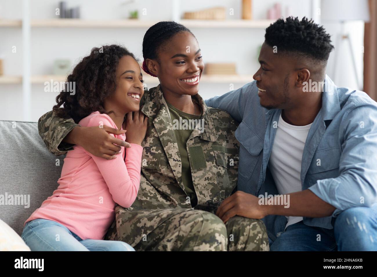 Donna nera amorevole in uniforme camouflage avendo conversazione con la famiglia Foto Stock