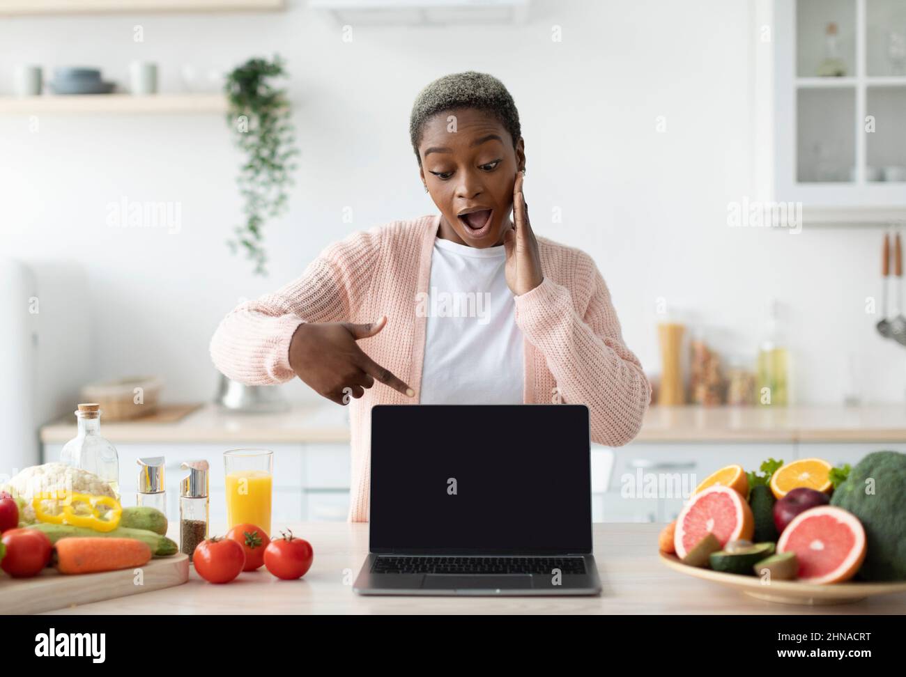 Scioccata signora americana africana millenaria con bocca aperta punta dito al computer portatile con schermo vuoto Foto Stock