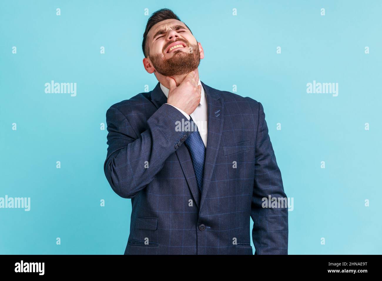 Dolore alla gola. Ritratto di infelice uomo d'affari malato indossare tuta ufficiale di stile che tocca il suo collo, soffrendo mal di gola, infezione virale o sintomi influenzali. Studio interno girato isolato su sfondo blu. Foto Stock