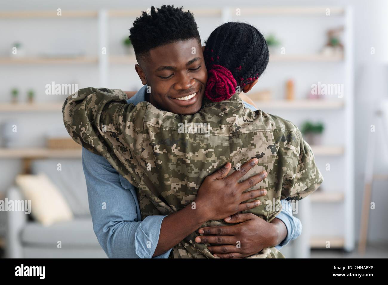 Felice famiglia nera moglie militare e marito abbracciare a casa Foto Stock