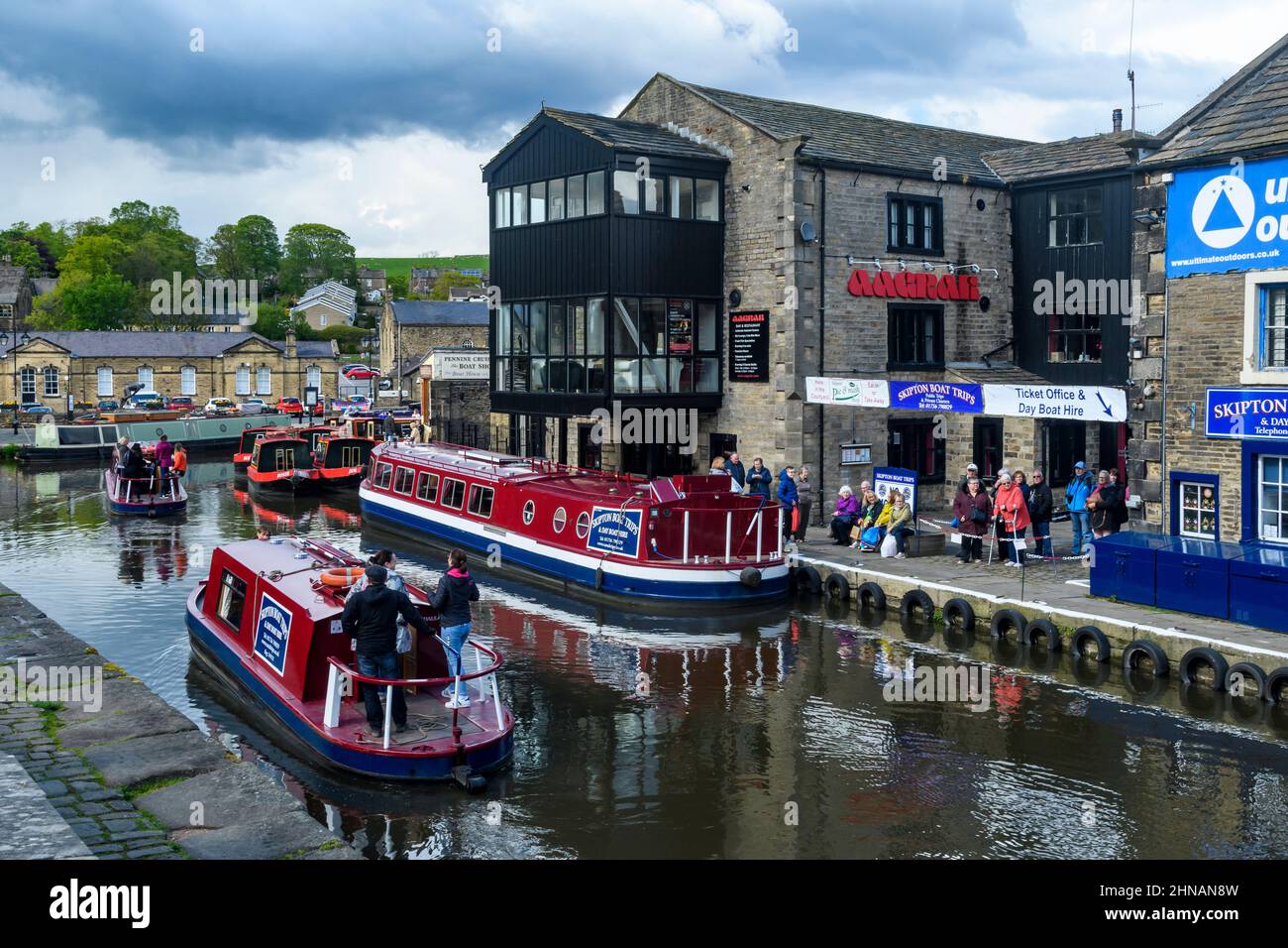 Gita turistica in acqua (uomini donne, auto-drive barca a noleggio rossa, clienti in coda, ormeggi) - panoramico Leeds-Liverpool Canal, Yorkshire, Inghilterra Regno Unito Foto Stock