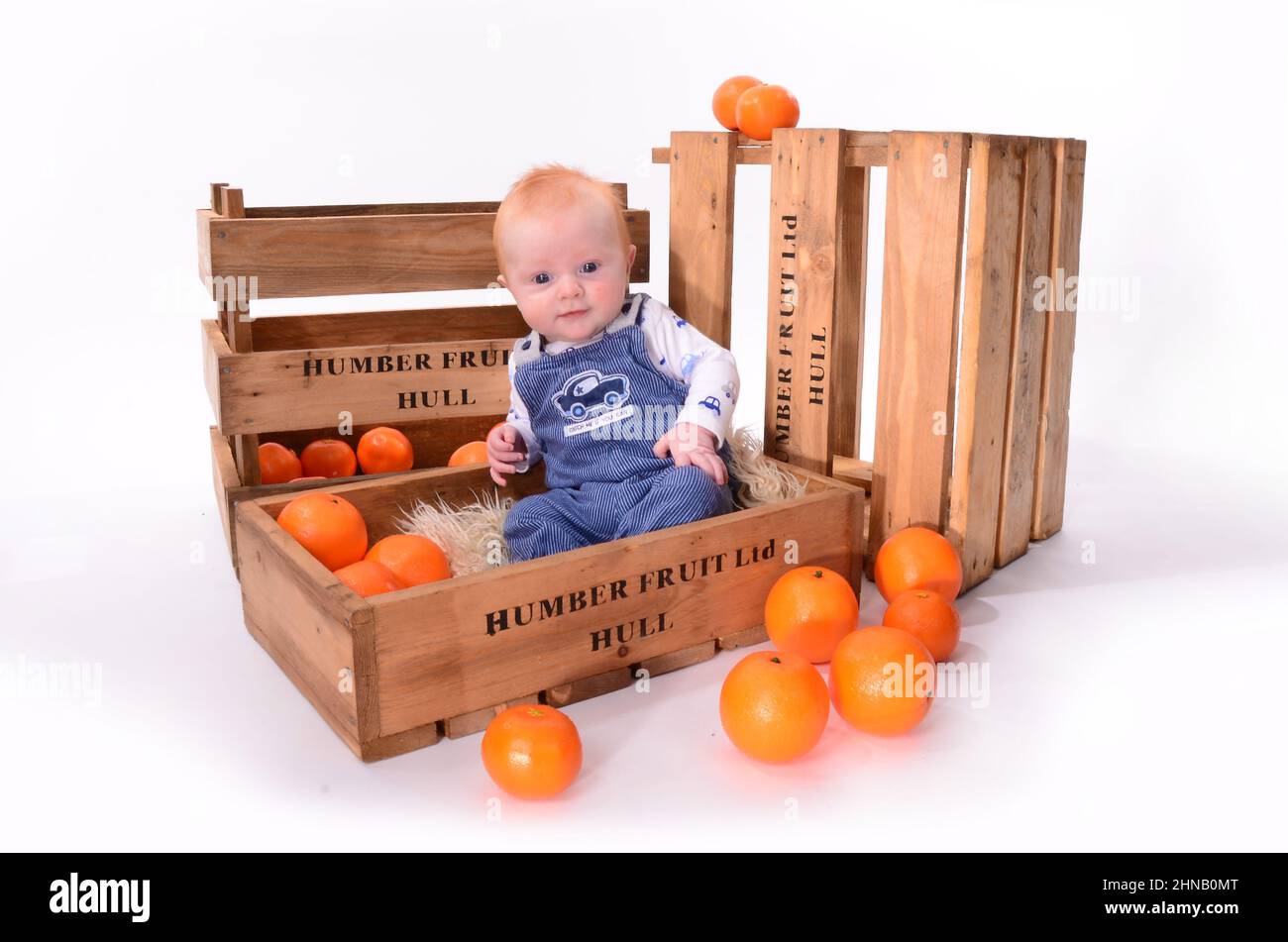 Ragazzo felice con capelli rossi che giocano in una scatola di frutta arancione Foto Stock