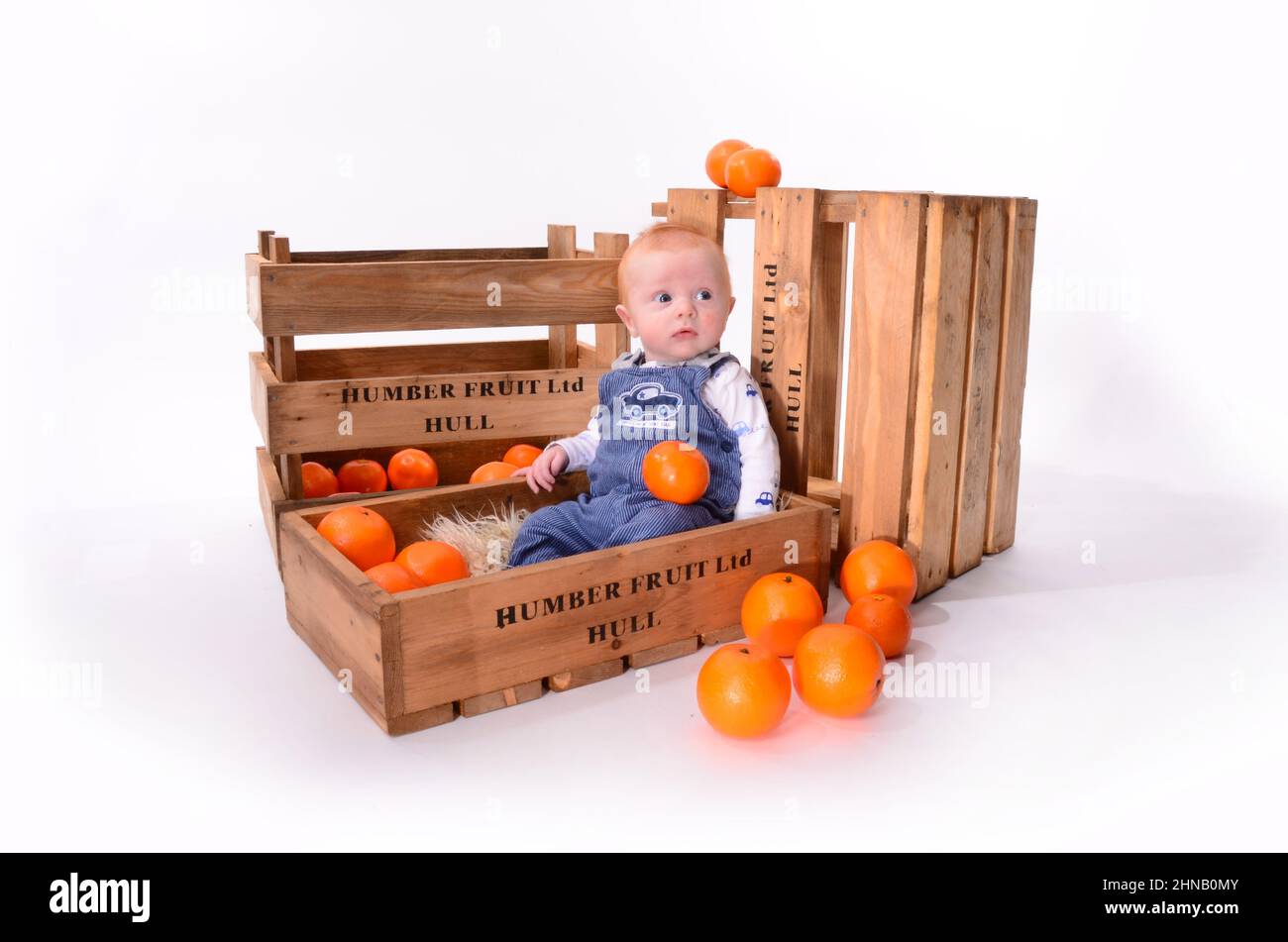 Ragazzo felice con capelli rossi che giocano in una scatola di frutta arancione Foto Stock