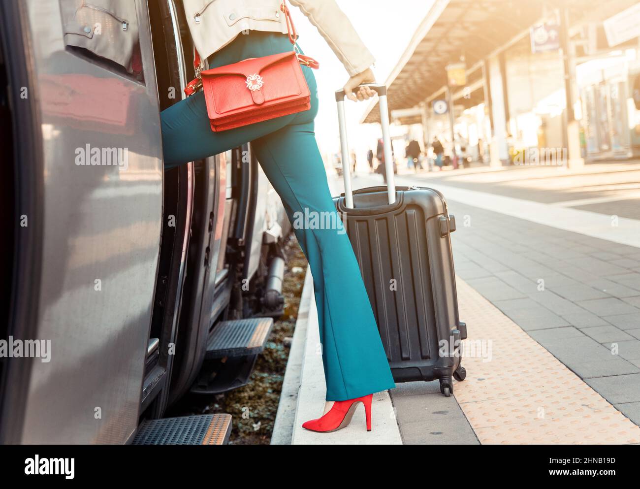 Il primo piano di gambe di una donna d'affari che si prende sul treno con borsa e carrello borsa - Donna sulla piattaforma di una stazione ferroviaria, prendendo il suo treno Foto Stock