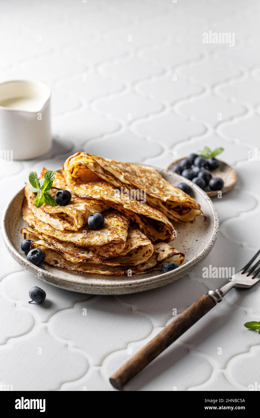 Deliziose crepes fatte in casa su piastra di ceramica con mirtillo e menta in composizione con crauti e forchetta su sfondo piastrellato bianco per mascenitsa. COP Foto Stock