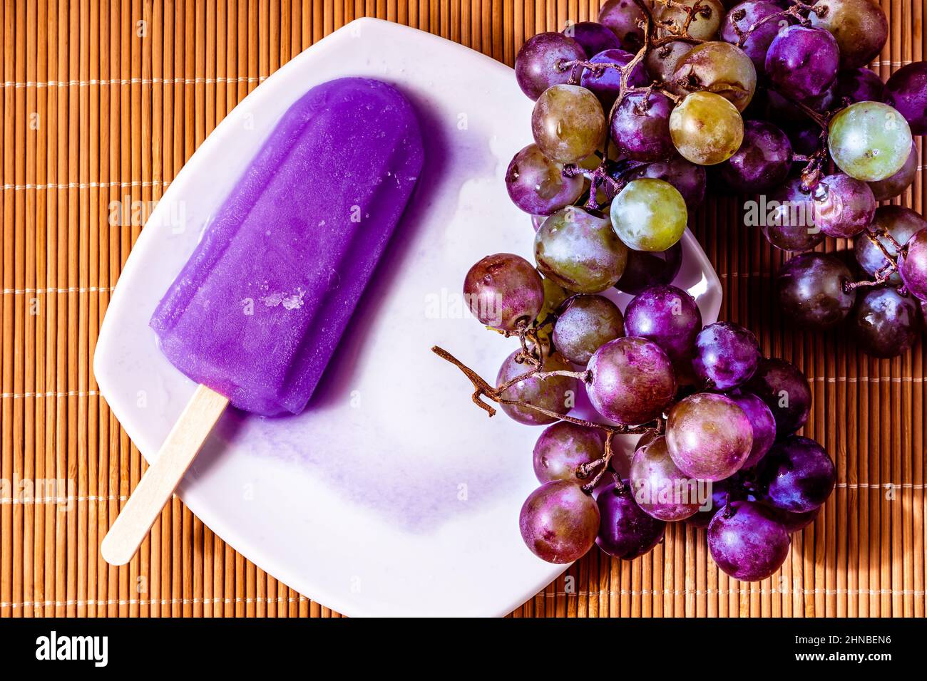 Un lecca lecca d'uva su un piccolo piatto bianco e uva viola su una superficie di bambo. Concetto di alimentazione naturale e salutare. CopySpace. Foto Stock