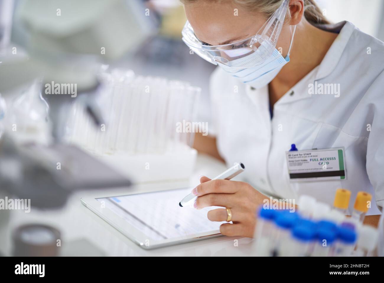 Prendere appunti per la sua tesi. Un giovane ricercatore che registra i suoi risultati su un tablet in laboratorio. Foto Stock