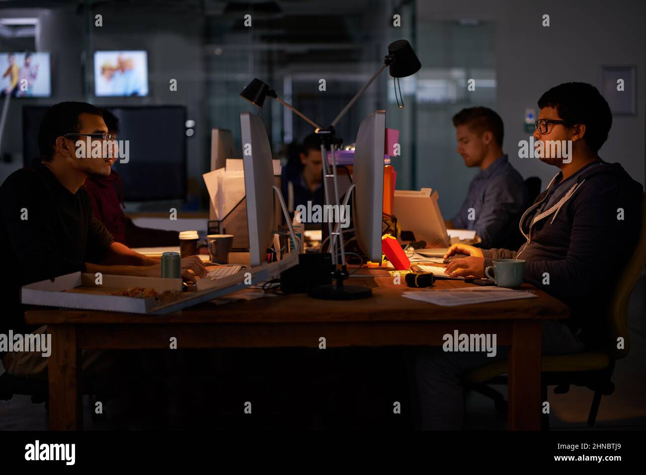 Esecuzione del lavoro. Scatto ritagliato di un gruppo di giovani colleghi che lavorano in un ufficio poco illuminato. Foto Stock