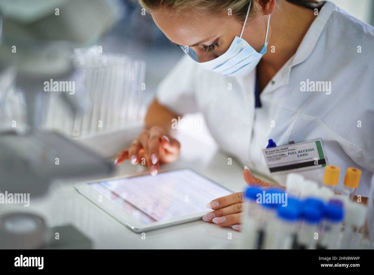 Controllo attraverso i suoi risultati. Un giovane ricercatore che registra i suoi risultati su un tablet in l suo laboratorio. Foto Stock