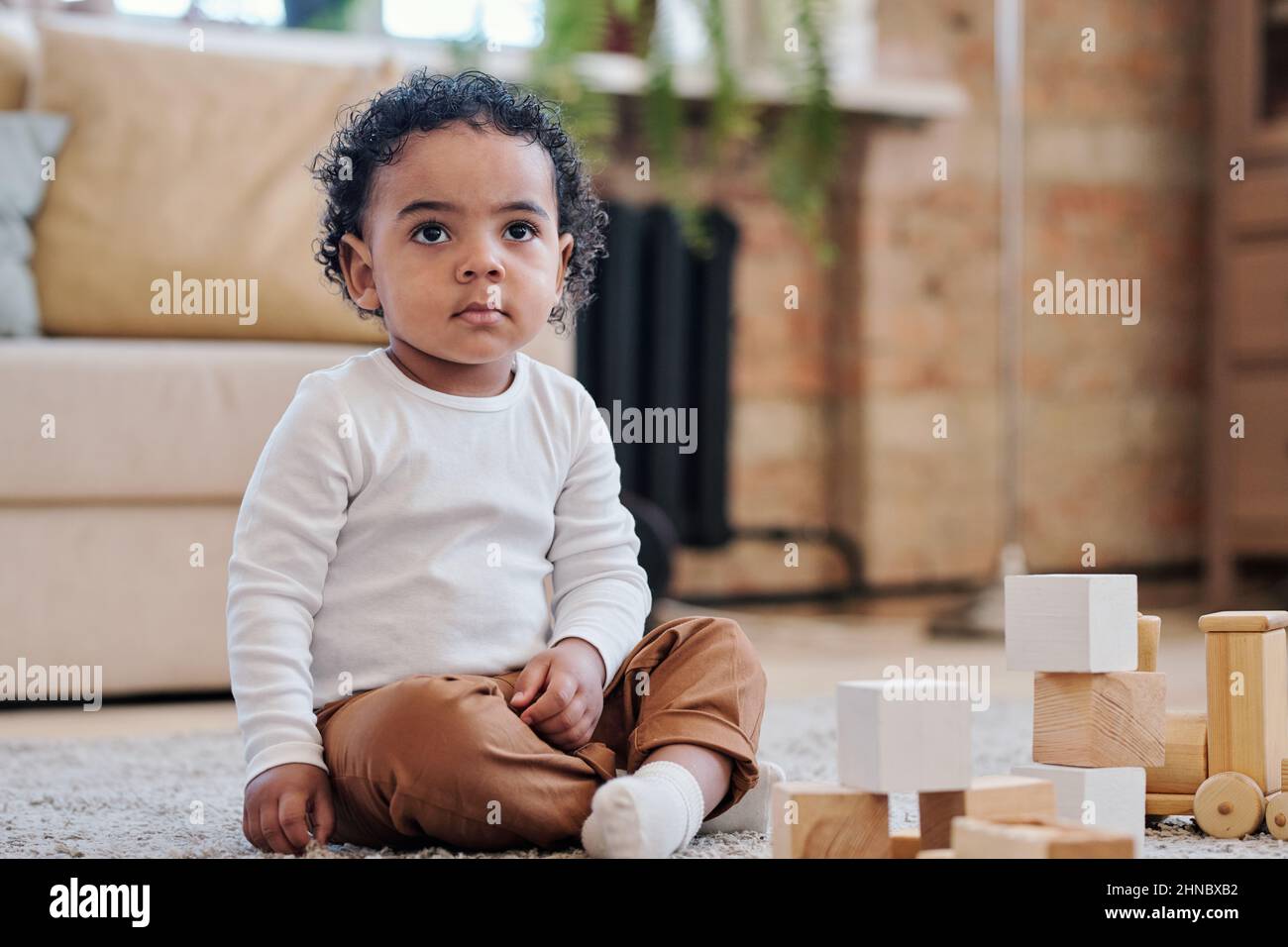 Bimbo nero concentrato con capelli ricci seduti su tappeto e giocando con i soli giocattoli Foto Stock