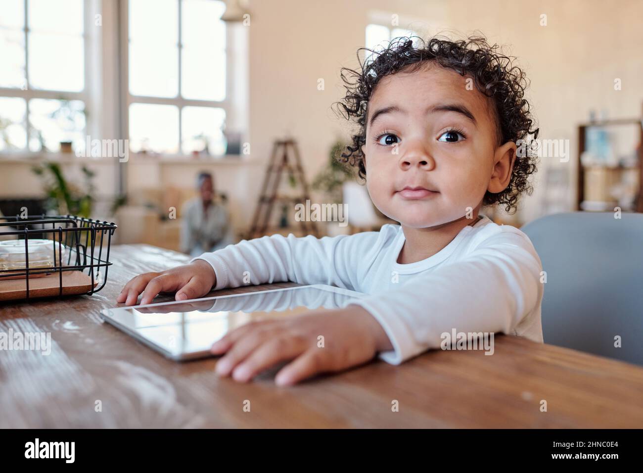 Ritratto di sorpreso curioso ragazzo afroamericano con capelli ricci seduti a tavola con gadget Foto Stock