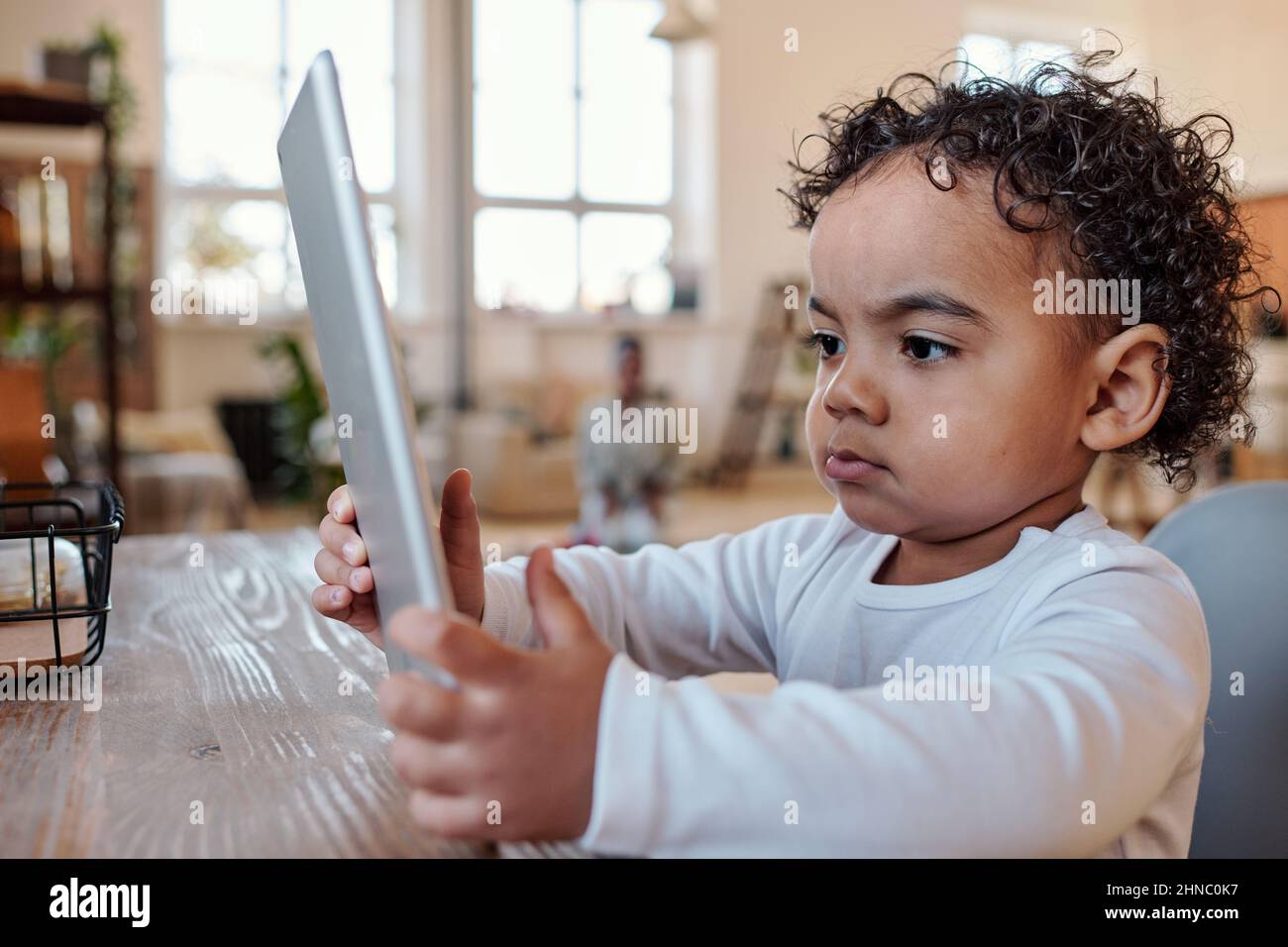 Bimbo afro-americano concentrato con capelli ricci seduti al tavolo e con l'app tablet Foto Stock