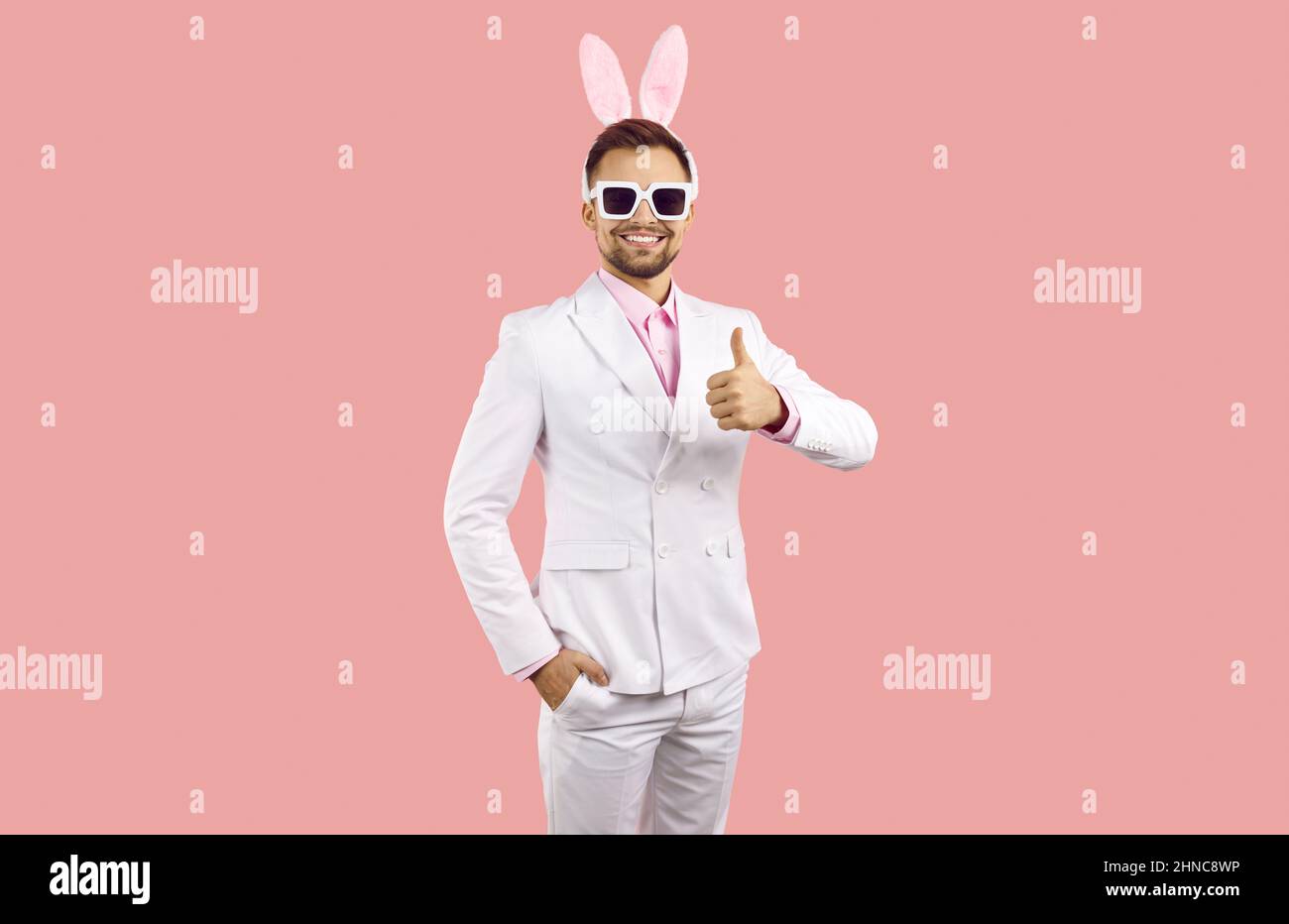 Felice bel ragazzo giovane in vestito e simpatico divertente pasqua coniglietto orecchie mostrando i pollici in su Foto Stock