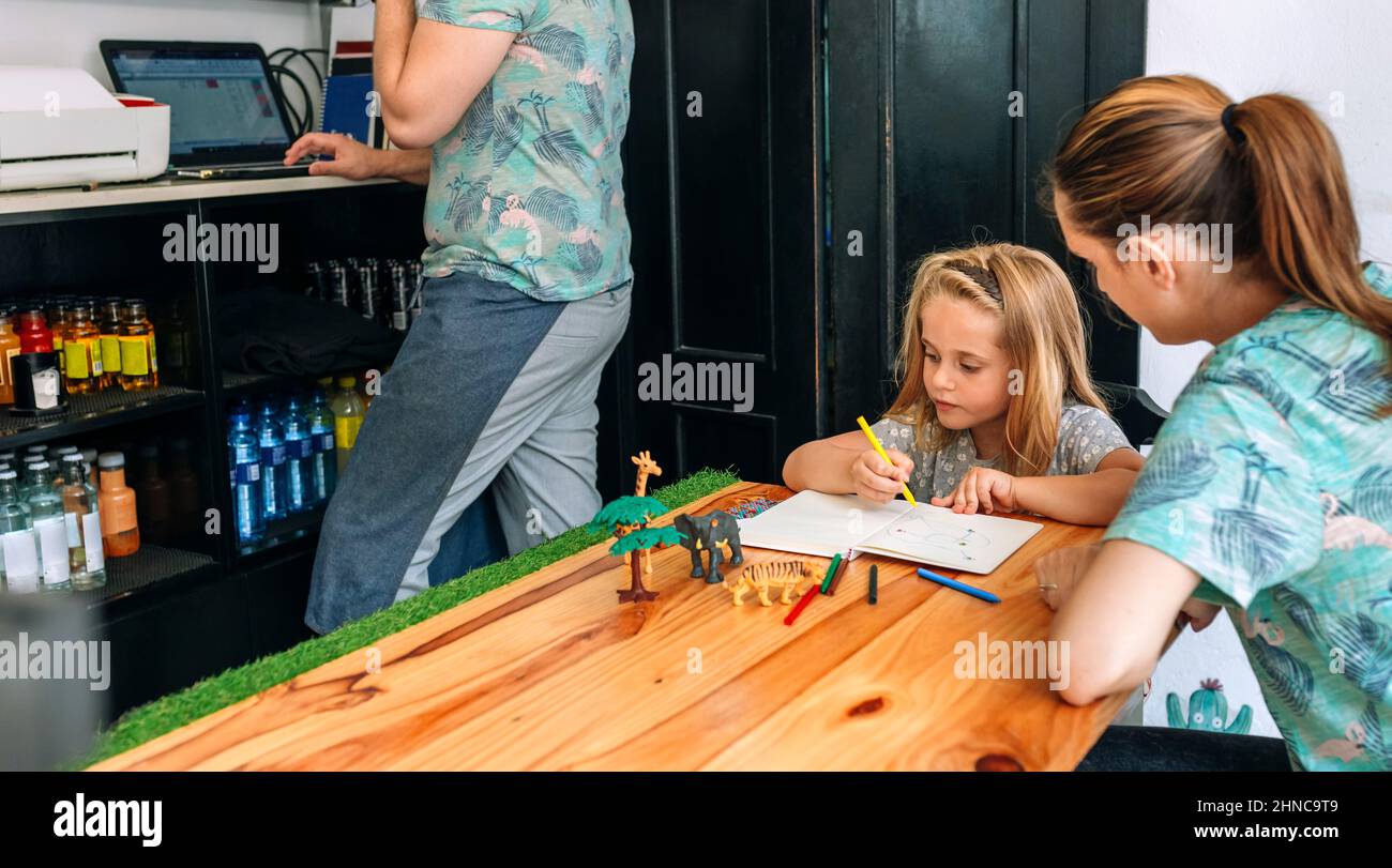 Madre che disegnano con sua figlia mentre il padre lavora nel loro caffetteria privata Foto Stock