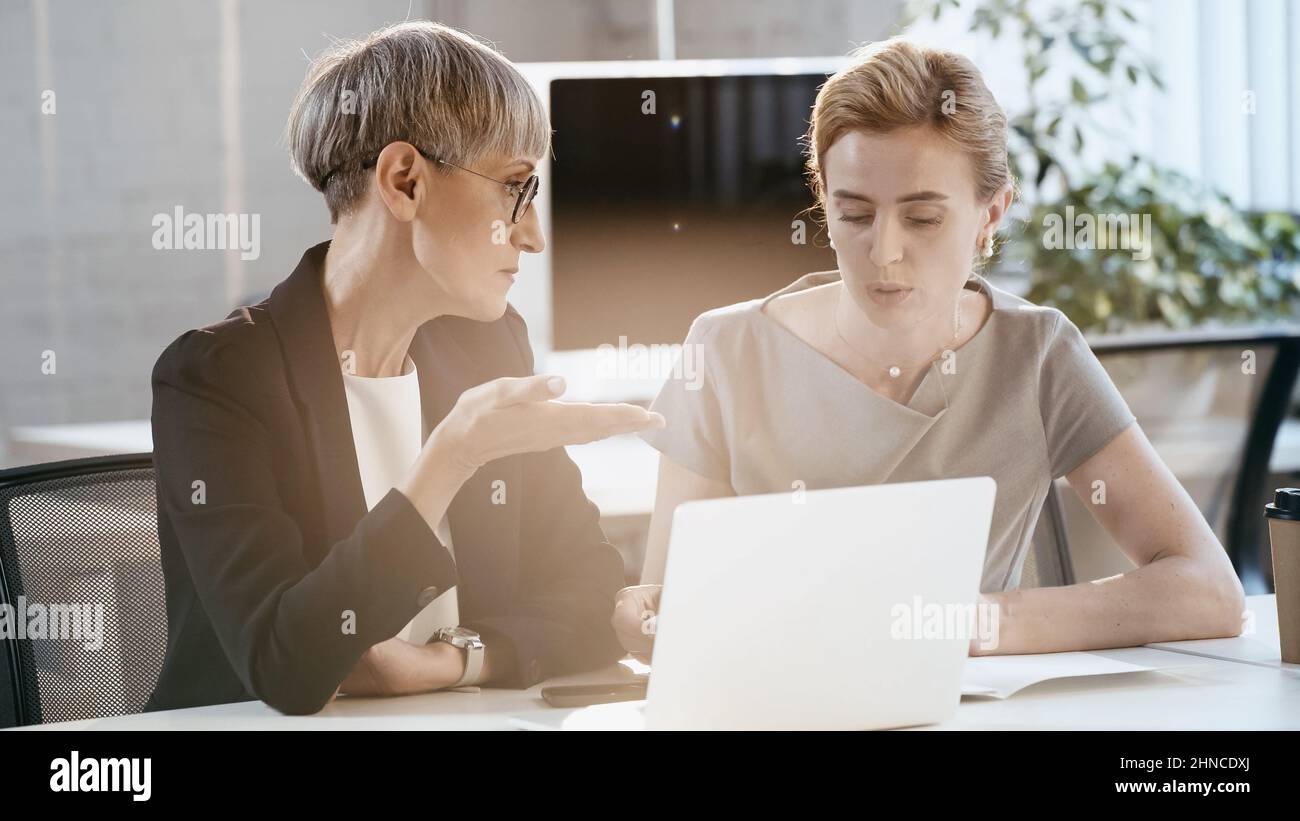Donna d'affari matura che punta con mano vicino a colleghi e dispositivi in ufficio Foto Stock