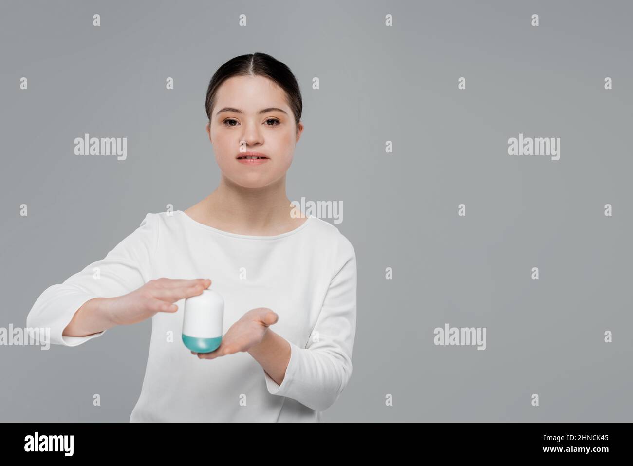 Donna con sindrome di Down che tiene deodorante isolato sul grigio Foto Stock