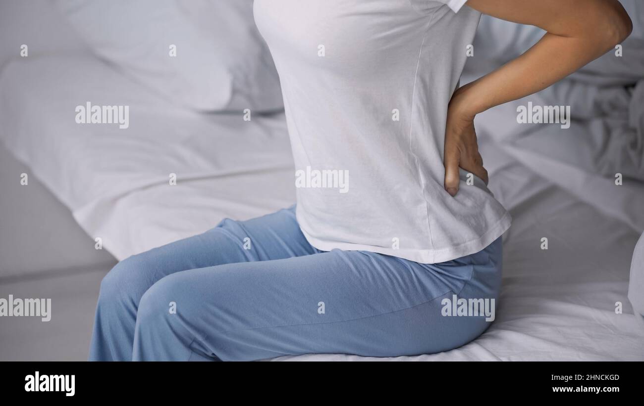 vista ritagliata della donna in pigiama seduta a letto e che soffre di male nella schiena Foto Stock