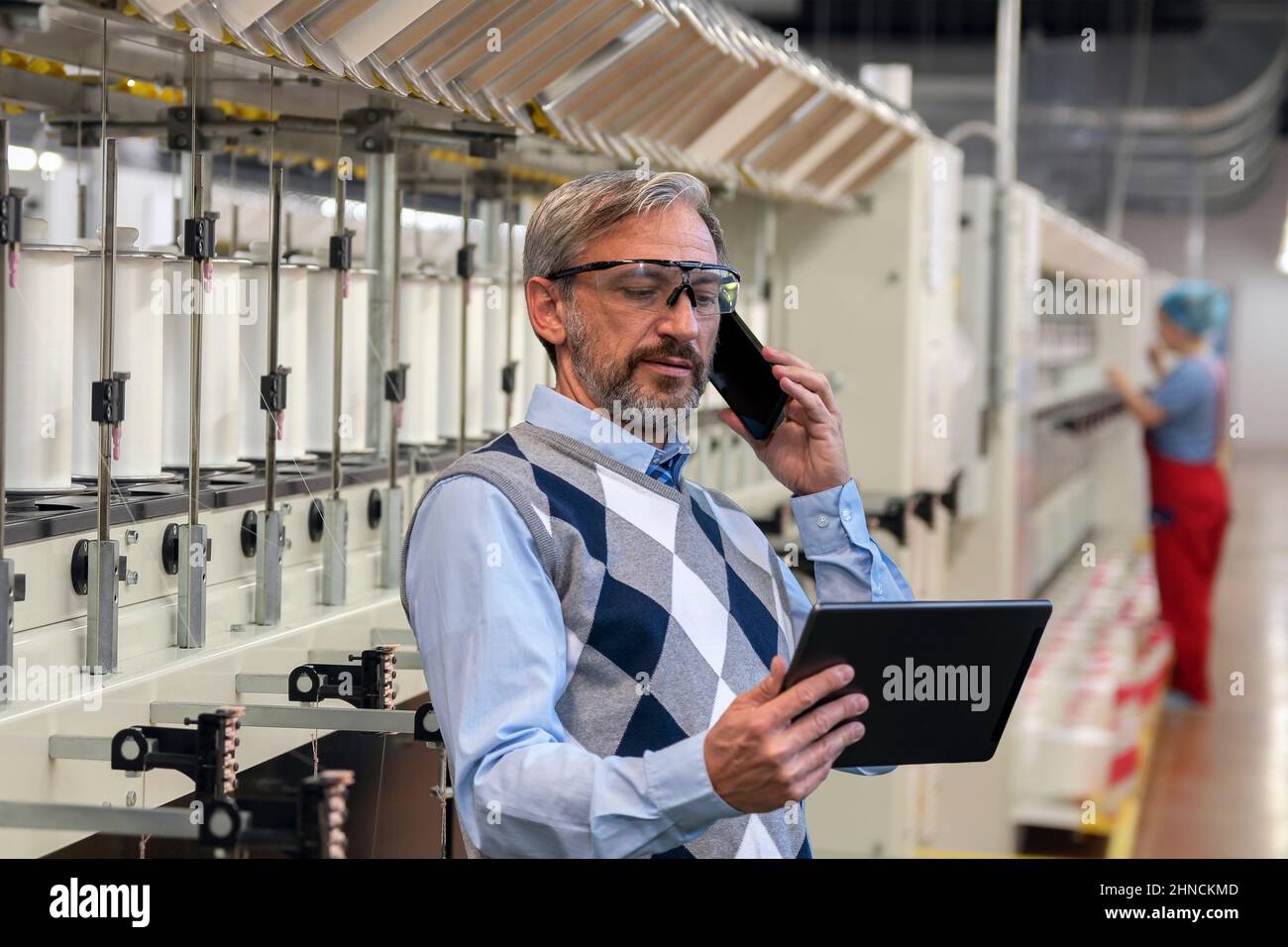 Vita in su Ritratto di uomo d'affari sicuro, bello, grigio-pelato. Uomo in piedi e utilizzando smartphone e tablet digitale . Foto Stock