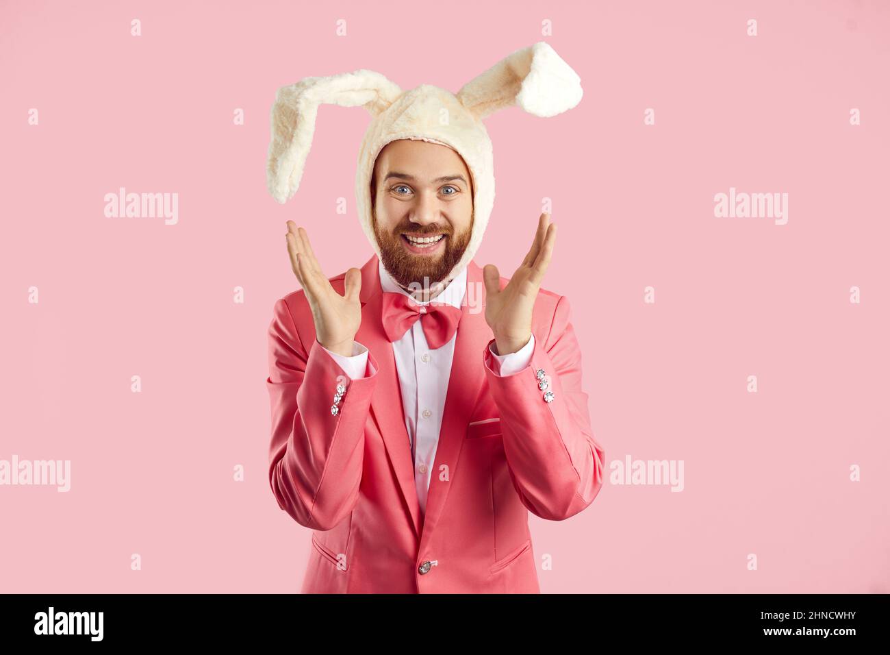 Positivo divertente uomo in morbido cappello bianco con orecchie di coniglio che è sinceramente felice su sfondo rosa. Foto Stock