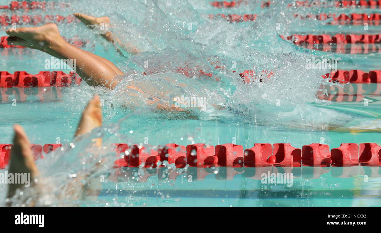 Gli atleti si tuffano in piscina per una gara di nuoto. Spashing acqua come i loro corpi entrano nelle corsie. Gambe e piedi in procinto di sommergere. Concorrenza Foto Stock