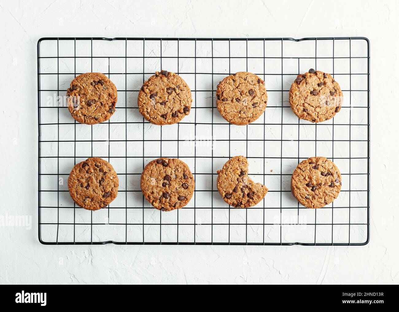 Vista dall'alto di gustosi biscotti dolci fatti in casa con gocce di cioccolato poste su una griglia di raffreddamento in metallo su sfondo bianco in cucina Foto Stock