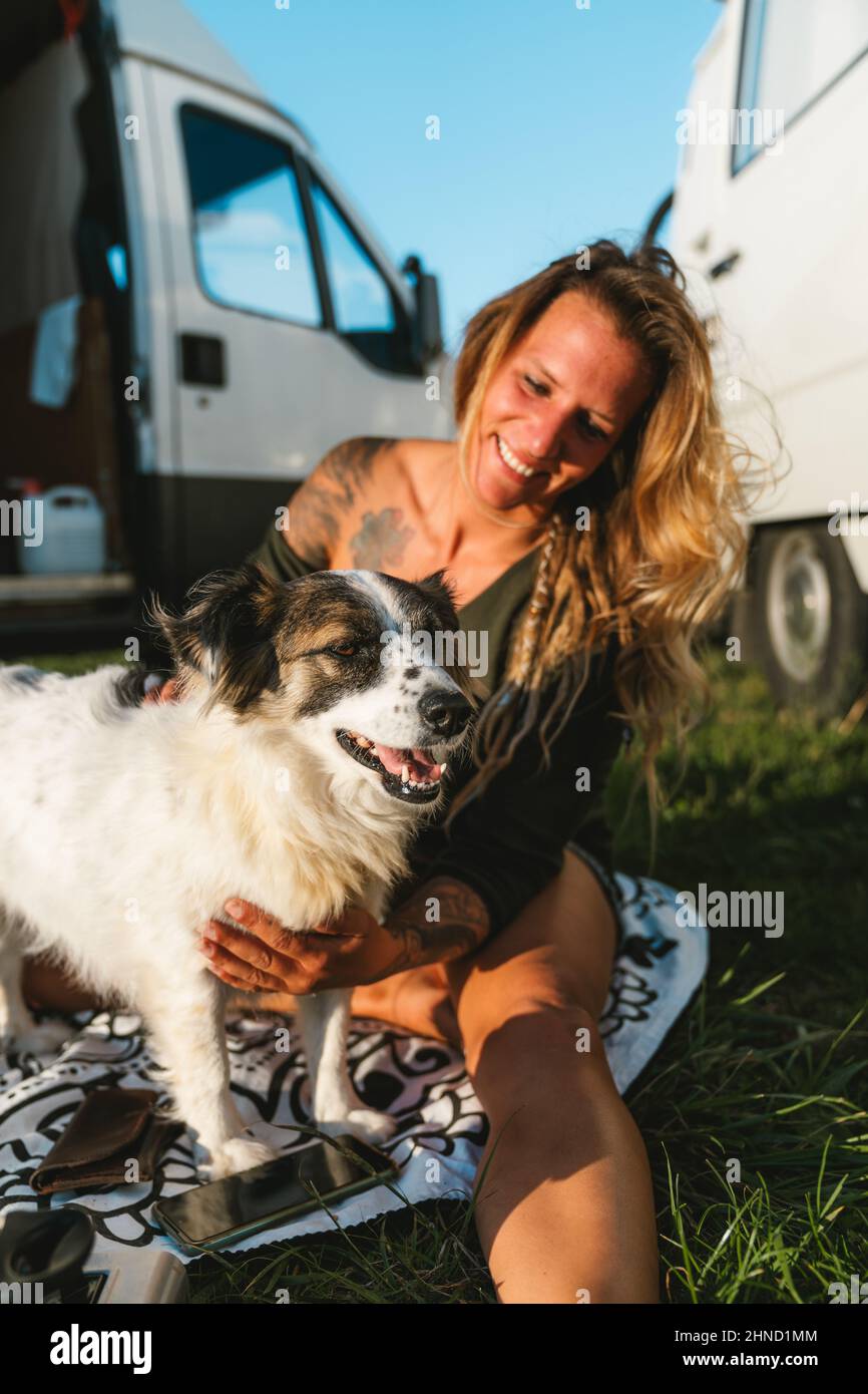 Positiva donna proprietario abbracciando carino peloso australiano Shepherd cane con muso avvistato mentre seduto su strada soleggiata il giorno d'estate Foto Stock