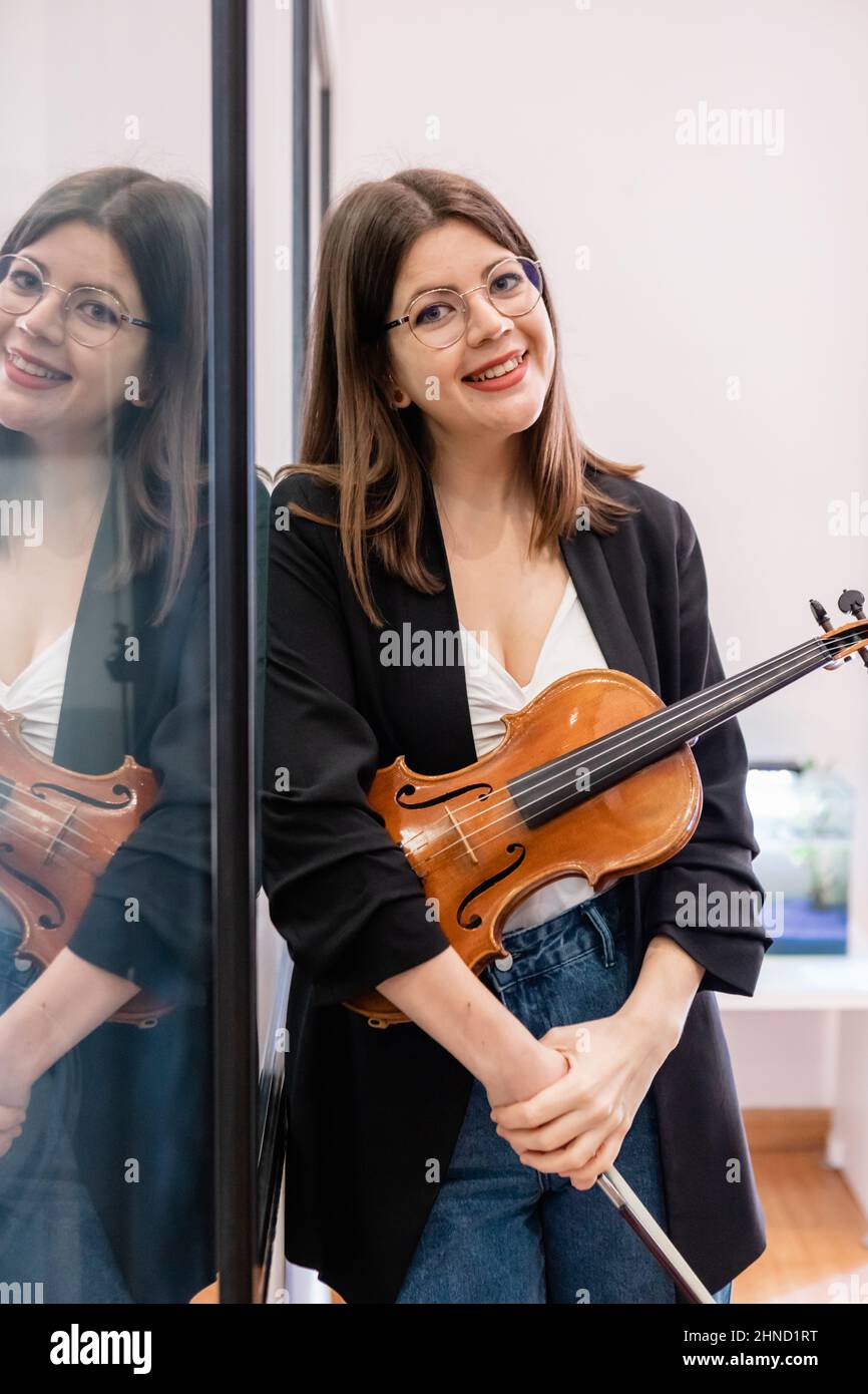 Allegra studentessa femminile in piedi con violino e arco in classe di scuola di musica e guardando la macchina fotografica Foto Stock